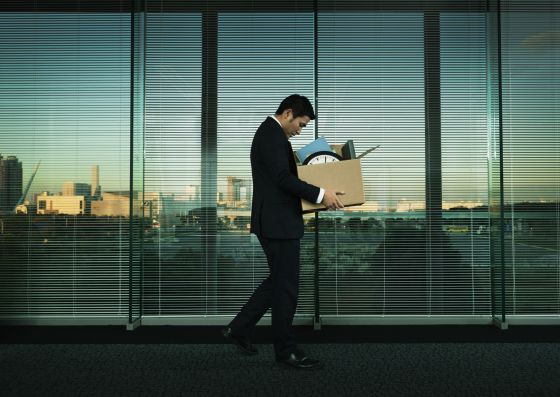 A sad man walking as he leaves a workplace holding a box of his office belongings