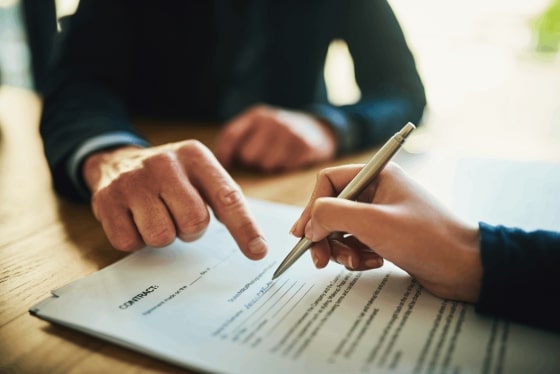 Woman signing a document as a man points to a place on the paper