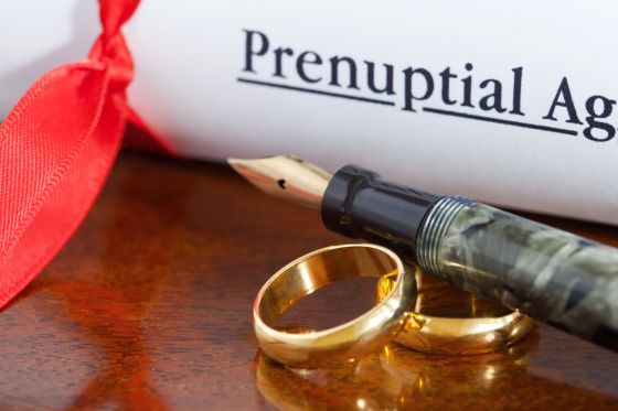 Prenuptial agreement rolled up and tied with a red ribbon next to 2 gold wedding bands and an ink pen