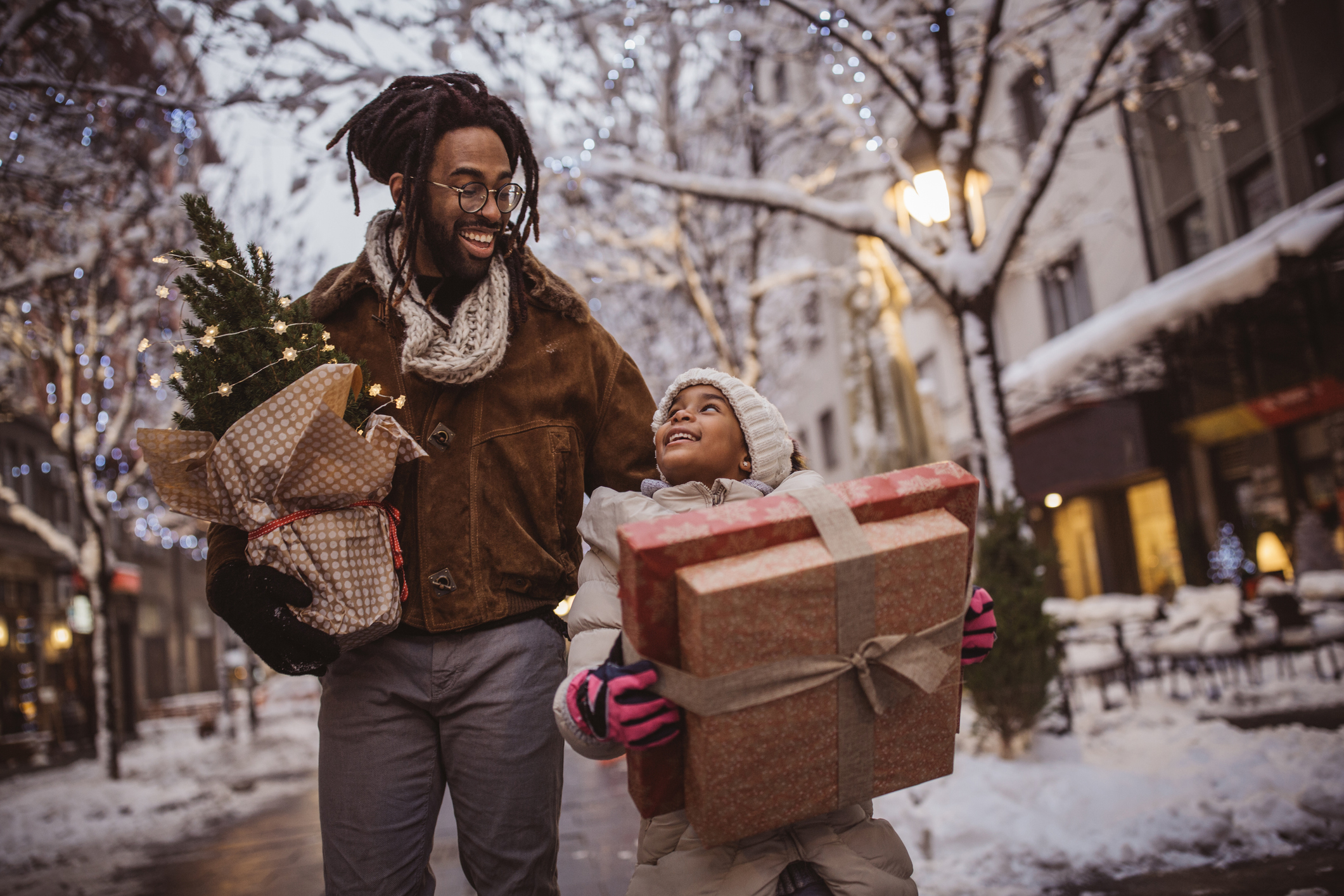 Young family preparing for Christmas holiday. They walking on street and holding gift boxes and Christmas tree